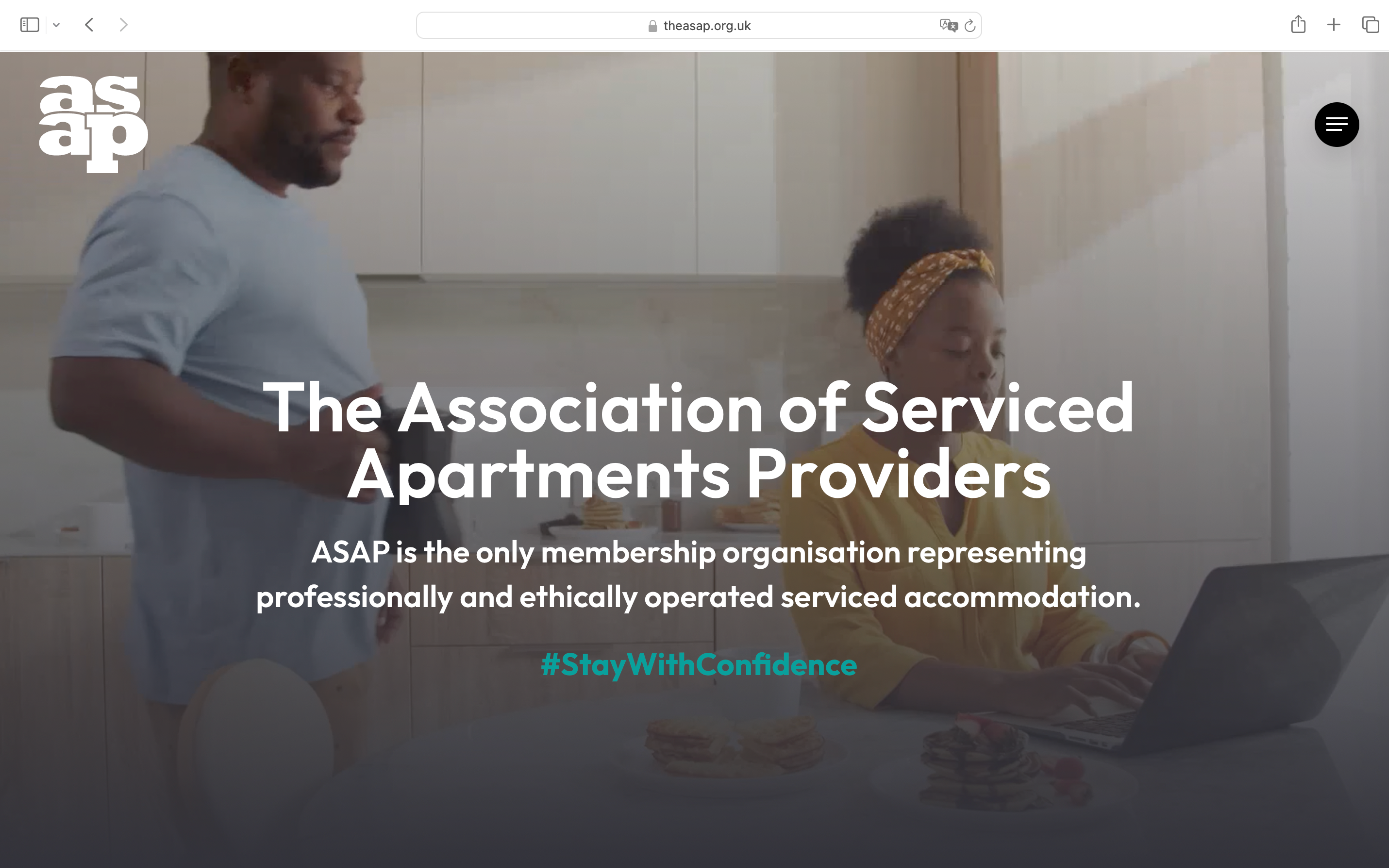 A screenshot of the new version of The ASAP's homepage, with an image of a Black man standing in a kitchen while a Black woman is sitting on a chair and typing on a laptop. The man is looking at the laptop screen and holding a mug in his right hand. The title "The Association of Serviced Apartments Providers" is shown in white, big and bold font across the page. Underneath, the text "ASAP is the only membership organisation representing professionally and ethically operated serviced accommodations" are shown in a white text box above the image of the apartment, with the text in white. Under this is, the hashtag "#StatWithConfidence" is shown in light blue font. The ASAP logo appears on the left hand corner of the page in white font, while the menu button appears on the right as a black circle with three white lines across it.